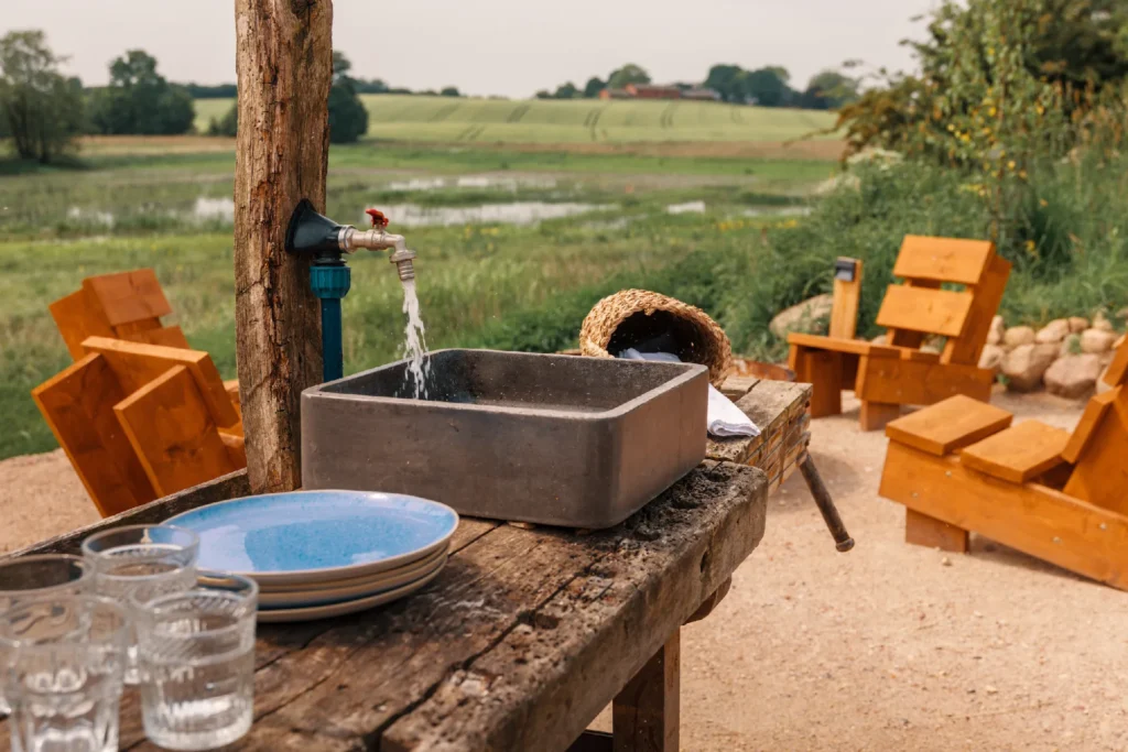 BBQ-Platz River: Holztisch mit Steinwaschbecken, Wasserhahn und Geschirr, Hof Bissee