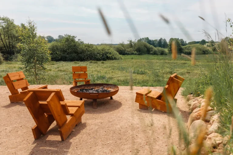 Sitzbereich mit Holz-Liegestühlen um eine Feuerschale am Wiesenrand, Hof Bissee