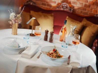 Table laid for two with risotto and rosé in front of a red velvet sofa in the restaurant, Hof Bissee